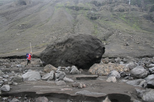 vísindamaður stendur við stórt bjarg í urðinni